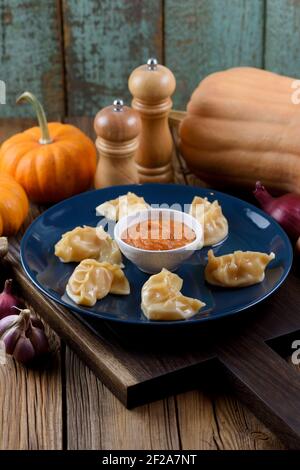 Plat asiatique traditionnel. Boulettes imparfaites en forme de croissant avec sauce épicée, servies avec de l'ail, de l'oignon et de la citrouille sur une planche de chêne, vue verticale Banque D'Images