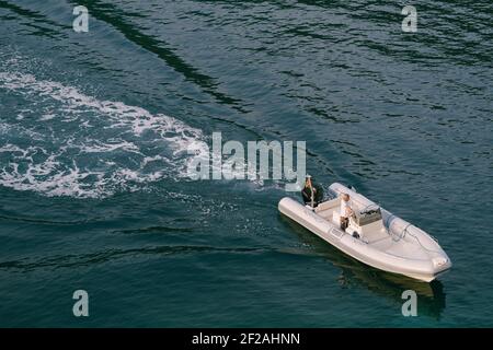 Un bateau en caoutchouc gris flotte sur la mer. Un homme dans un T-shirt blanc conduit un bateau. Vue de dessus d'un bateau à voile à moteur. Banque D'Images