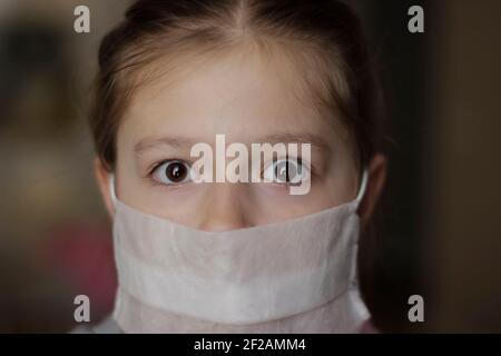Petite fille européenne portant un masque pour protéger les p2,5 et Covid-19. Enfant malade les petites filles regardent la caméra posant dans le studio dans une robe rouge avec Banque D'Images