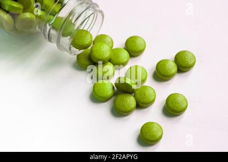 Des pilules et des comprimés verts végétariens débordent de la pilule en verre bouteille sur fond blanc Banque D'Images