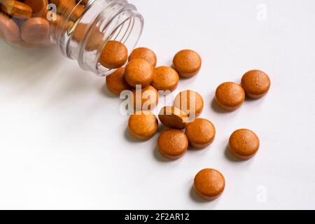 Des comprimés et des comprimés d'orange brun qui se répandent de la pilule de verre bouteille sur fond blanc Banque D'Images