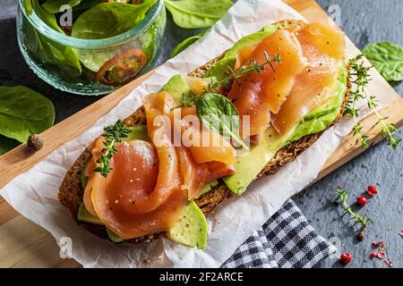 Saumon fumé appétissant et sain avec avocat et légumes (pousses d'épinards, tomates, thym) sur le pain grillé. Style maison. Vue de dessus. Banque D'Images