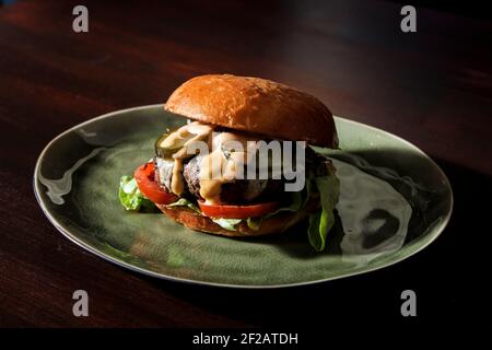 Hamburger de bœuf juteux classique avec tranches de tomates, concombres marinés, fromage et sauce légère et laitue sur un petit pain maison Banque D'Images