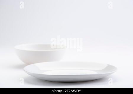 Articles de table blancs, différentes formes d'un bol en céramique blanc vide et d'une assiette disposés sur un fond blanc texturé. Banque D'Images