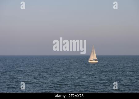Un seul bateau navigue à travers l'immensité de la mer le soir ensoleillé, minimalisme, bleu eau et ciel, horizon au-dessus de la mer, voilier, moitié et moitié, ciel Banque D'Images