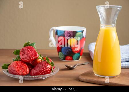 Vue sur une assiette de fraises, bouteille de jus d'orange, tasse de couleur, cuillère et tissu sur table en bois, pour le petit déjeuner, horizontal Banque D'Images