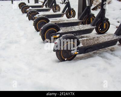 Transport urbain électrique: La rangée de lectures électriques pour monter des motos de scooter avec des accumulateurs garés dans la neige en hiver. Banque D'Images