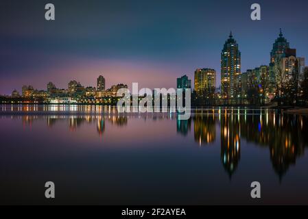 Vue nocturne des bâtiments modernes dans le quartier Obolon de Kiev, Ukraine, près du fleuve Dnieper, les lumières se reflètent sur l'eau calme. Banque D'Images