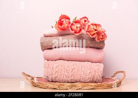 Une pile de chandails tricotés pour femmes sur un plateau en osier sur une étagère, à côté d'un bouquet de fleurs Banque D'Images