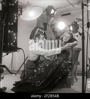 photographe et mannequin de mode des années 1940. Une jeune femme modèle est dans un studio de photographes reçoit quelques instructions finales avant de prendre les photos. Les lampes et la caméra sont visibles. Suède 1949 réf. AT7-6 Banque D'Images