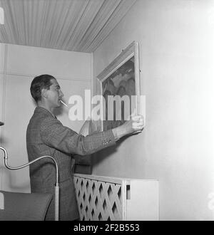 Dans les années 1940. Un homme essaie de mettre un tableau sur le mur et l'ajuste soigneusement de sorte qu'il pend droit. Suède 1944 réf. H83-3 Banque D'Images