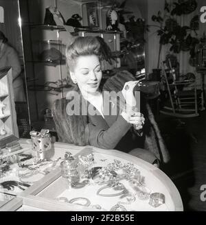 Shopping dans les années 1940. Une jeune femme dans un magasin avec une sélection de bijoux et de charmes. Sur le comptoir des produits de Svensk tenn. Elle essaie un bracelet argenté. Suède 1946 réf. X122-1 Banque D'Images