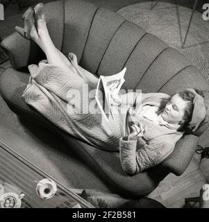 Femme des années 1940. Une jeune femme dans le salon est confortablement couché sur le canapé lisant un magazine et fume une cigarette. Elle semble très content dans la situation et a ses pieds sur l'accoudoir. Elle porte une robe de chambre ou une robe de chambre agréable et confortable. Suède 1947. Kristoffersson réf. AB3-6 Banque D'Images