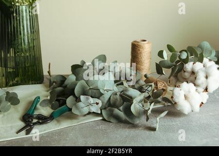 Concept floristique avec eucalyptus, fleurs blanches, coton et ficelle sur une table grise, flat lay douillet Banque D'Images