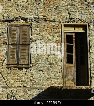 Façade traditionnelle de maison rurale avec un mur en pierre, une ancienne porte en bois et des volets de fenêtre altérés dans l'île de Karpathos, Dodécanèse Grèce. Banque D'Images