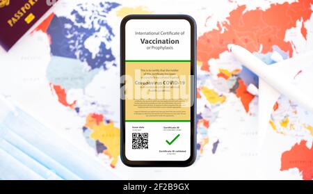 Un smartphone avec un certificat de vaccination contre le Covid-19 est organisé sur une carte du monde floue. Banque D'Images