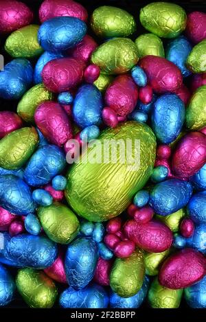 Pile ou groupe de plusieurs couleurs et différentes tailles d'oeufs de pâques au chocolat enveloppés d'une feuille colorée en rose, bleu, jaune et vert lime. Banque D'Images