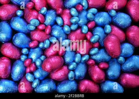 Pile ou groupe de plusieurs couleurs et différentes tailles d'oeufs de pâques au chocolat enveloppés de papier d'aluminium coloré en bleu et rose. Banque D'Images