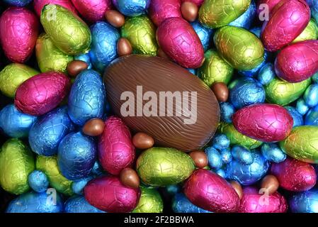 Pile ou groupe de plusieurs couleurs et différentes tailles d'oeufs de pâques au chocolat enveloppés d'une feuille colorée en bleu, rose, rouge, jaune et vert lime. Banque D'Images