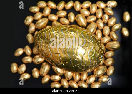 Pile ou groupe de plusieurs couleurs et différentes tailles de œufs de pâques au chocolat, enveloppés d'une feuille colorée, en or et en argent avec un grand chocolat au lait d'or Banque D'Images