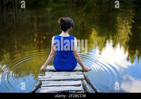 Vue arrière d'une femme en robe bleue assise sur un quai en bois au bord d'un lac, Bulgarie Banque D'Images