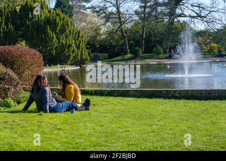 Deux dames s'assoient sur l'herbe, appréciant la nature et l'étang au Pinner Memorial Park. Pinner, Harrow, Londres. Banque D'Images