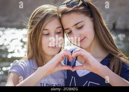 Deux adolescentes en plein air formant la forme du cœur avec leurs mains Banque D'Images