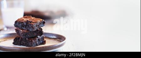 Bannière de brownies fudgy maison fraîchement faites empilés sur une soucoupe au-dessus d'une table en bois rustique blanc. Faible profondeur de champ avec arrière-plan flou. Banque D'Images