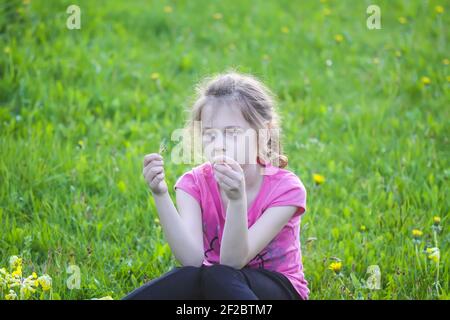 Une fille assise sur l'herbe verte dans le jardin de printemps. Enfant explorant la nature. Banque D'Images