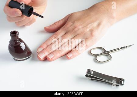 Femme se manucure. Mains de femmes, tenant la brosse pour vernis à ongles, les ciseaux et les coupe-ongles sur fond blanc. Banque D'Images