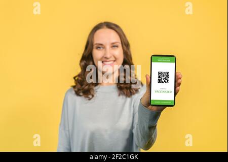 Accent sélectif sur l'écran du smartphone avec un passeport covid en main d'une femme isolée sur la confirmation jaune de la vaccination du coronavirus, Voyage après la pandémie concept Banque D'Images