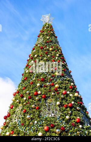 Grand arbre de Noël décoré en plastique avec des boules rouges et jaunes sur fond bleu ciel Banque D'Images