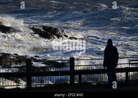 Vents forts et surf des tempêtes battent la côte à Mumbles Head. Un marcheur est arrêté dans ses pistes en admiration de la puissance des vagues. Banque D'Images