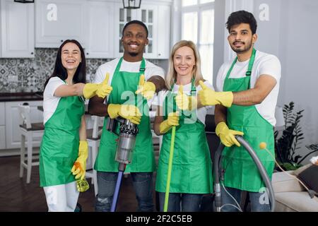 Une équipe de nettoyeurs professionnels souriants et multiraciaux qui se montre à la hauteur de vos pouces appareil photo Banque D'Images