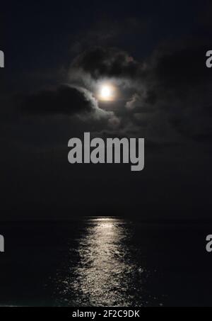 Une pleine lune brillante entre les nuages avec lumière de lune réfléchie sur la mer dans le sud de la France. Banque D'Images