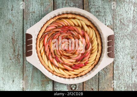 Tarte aux pommes maison en forme de rose avec remplissage de frangipane plat de cuisson sur fond texturé en bois bleu rustique au-dessus de la vue Banque D'Images