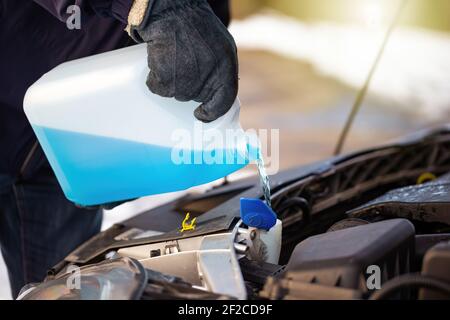 Homme remplissant de liquide de refroidissement antigel pour nettoyer la vitre avant avec de la neige en arrière-plan Banque D'Images