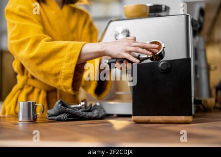 Femme en peignoir jaune qui prépare un expresso sur une machine à café professionnelle à la maison, en gros plan. Processus de préparation du café avec une machine à café. Banque D'Images