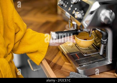 Femme en peignoir jaune qui prépare un expresso sur une machine à café professionnelle à la maison, en gros plan. Processus de préparation du café avec une machine à café. Banque D'Images