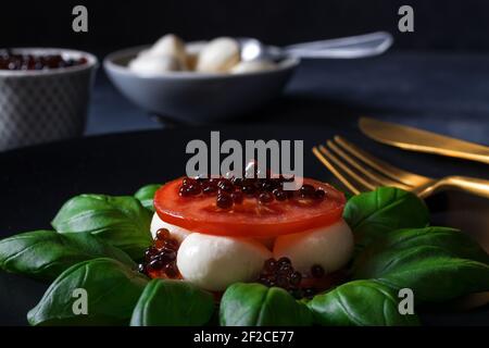 Variété de salade Caprese, tranches de tomates mûres fraîches, mini-mozzarella, feuilles de basilic frais et caviar balsamique. Tableau d'arrière-plan sombre. Gros plan v Banque D'Images