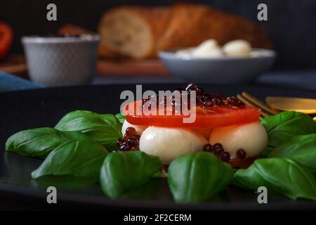 Variété de salade Caprese, tranches de tomates mûres fraîches, mini-mozzarella, feuilles de basilic frais et caviar balsamique. Tableau d'arrière-plan sombre. Haut vers le bas v Banque D'Images