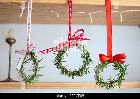 Trois couronnes de romarin ornées de rubans rouges festifs, suspendues à une étagère. Décoration naturelle, bricolage, idée pour Noël. Banque D'Images