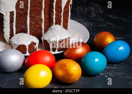 Gâteaux de Pâques artisanaux faits maison couverts de glaçage blanc et d'œufs de Pâques peints multicolores sur des assiettes sur fond sombre. Banque D'Images