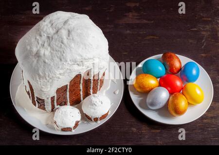 Gâteaux de Pâques artisanaux faits maison couverts de glaçage blanc et d'œufs de Pâques peints multicolores sur des assiettes sur un fond en bois sombre. Banque D'Images