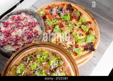 Assortiment de pizzas avec viande, salami, prosciutto, tomates, mozzarella, parmesan, salade, oignon bleu, œuf de caille sur des planches de bois. Vue de dessus. Banque D'Images