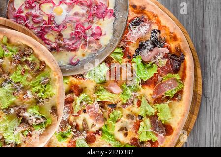 Assortiment de pizzas avec viande, salami, prosciutto, tomates, mozzarella, parmesan, salade, oignon bleu, œuf de caille sur des planches de bois. Vue de dessus. Banque D'Images