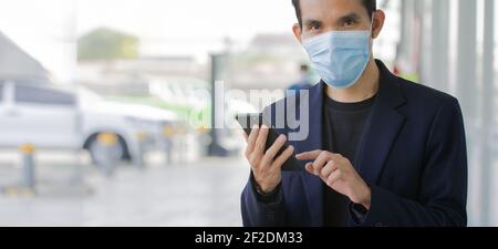 Homme d'affaires porter un masque médical utiliser smartphone regarder l'appareil photo extérieur, masque de protection du coronavirus covid19 Banque D'Images