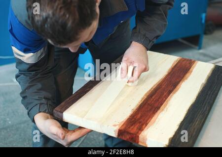 Un ébéniste travaille avec du bois dans un atelier de menuiserie. Un jeune travailleur d'apparence caucasienne fait un comptoir. Banque D'Images