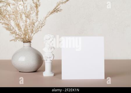 Carte en papier vierge, maquettes d'invitation avec petite statue et pampas d'herbe dans un vase sur fond blanc et beige. Décoration moderne. Espace copie Banque D'Images