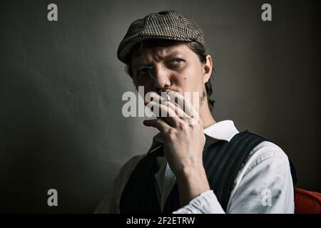 Un jeune homme fume une cigarette, souffle de la fumée, habillé dans un style rétro, dans un béret, une prise de vue cinématographique, gros plan Banque D'Images